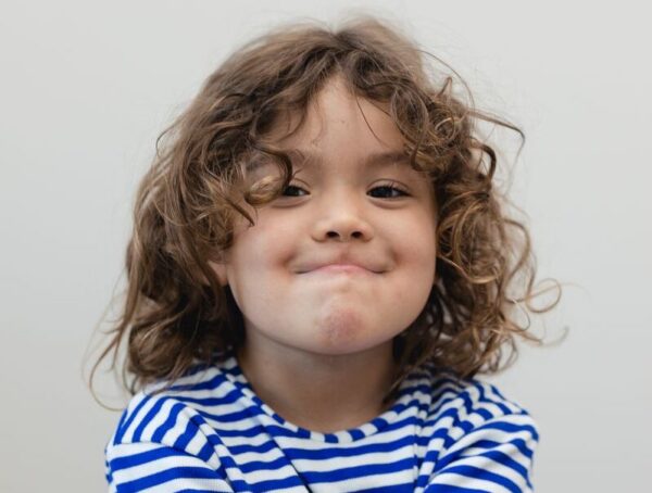 Barn med lockigt hår och blåvit randig tröja ler mot kameran.