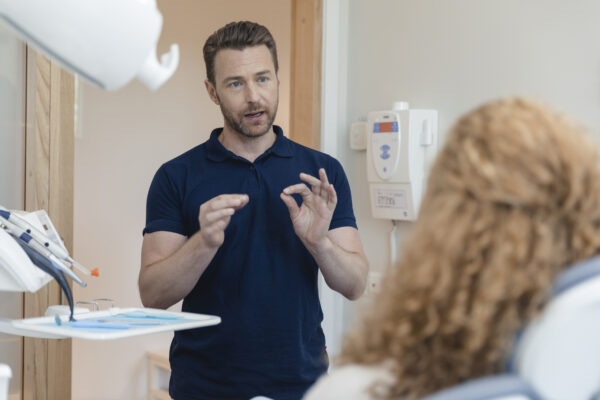 Tandläkare pratar med en patient som sitter i tandläkarstolen.